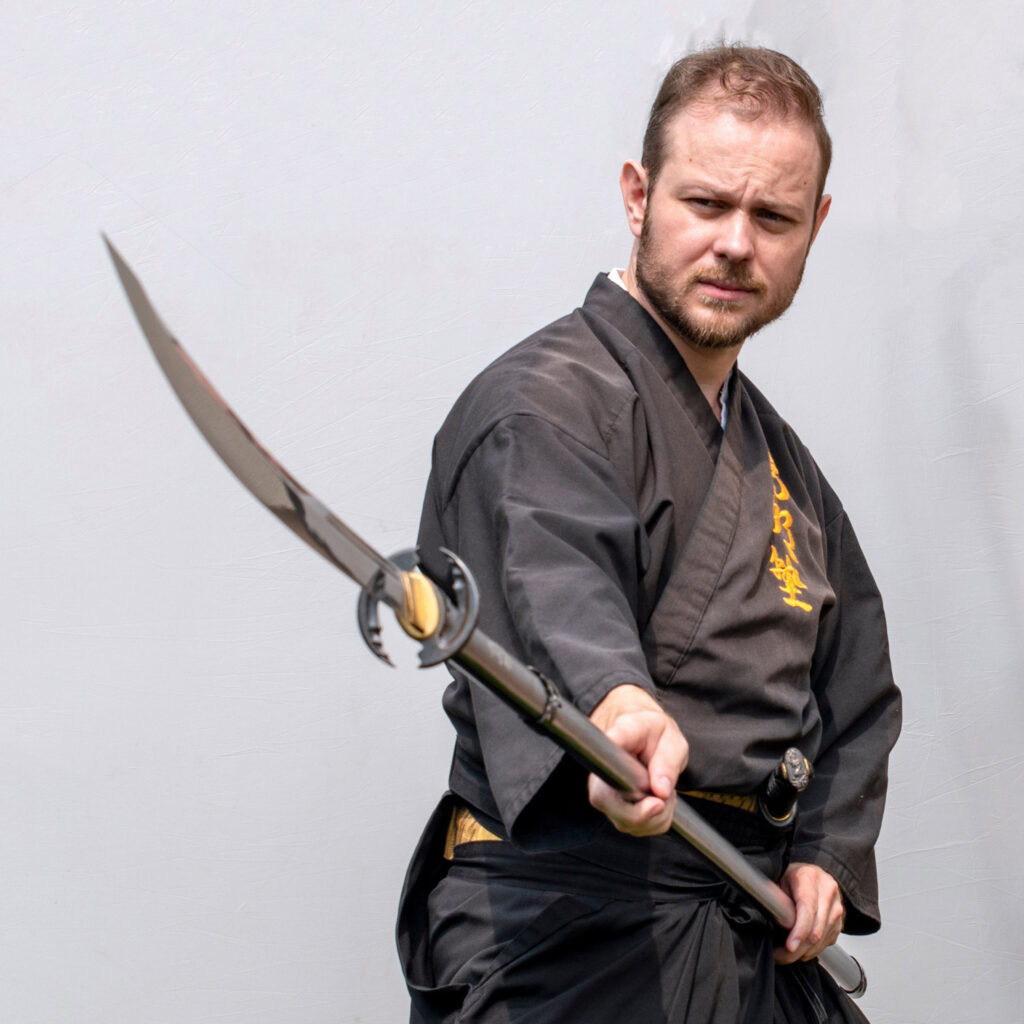 Sebastijan Sekol in Chudan-no-Kamae Stellung mit Naginata in schwarzer Uniform – Naginatajutsu Schwertkunst Graz